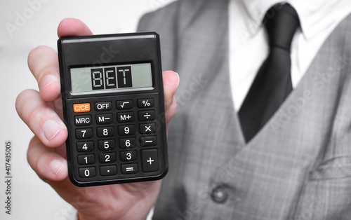 BET word text inscription on calculator in a male hand of a businessman in white shirt and blue tie, Concept of finance and banking. close up, banner.