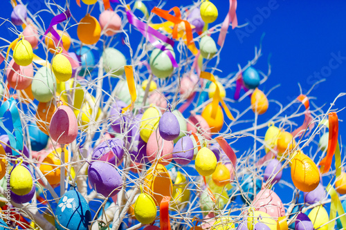 Colorful Easter eggs hang on a tree against the blue spring sky. Festive of city streets decoration for springtime holidays. Happy Easter.
