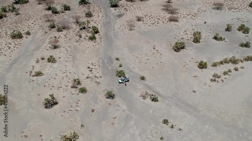  Looking down on a dry brown desert landscape with a off road vehicle in the middle of the shot camera moving away to very high veiwpoint Aerial Video photo