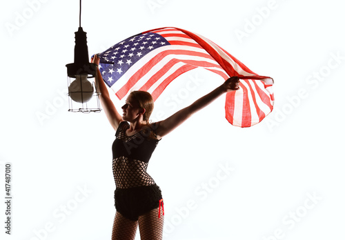 A patriotic teenage girl is seen in front
of a white background. She proudly waves the 
American flag around her in a cheerful manner.