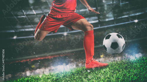 Close up of a soccer scene at night match with player in a red uniform kicking the ball with power