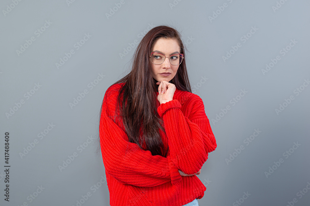 Fototapeta premium young emotional teenage female with glasses dressed in a red sweater posing on a gray background