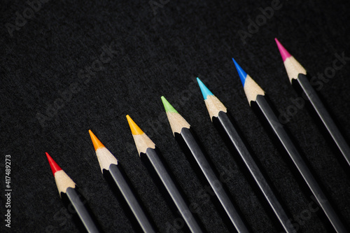 Sharpened wooden color pencils with black body color on the black felt solid fond background ordered in rainbow sequence