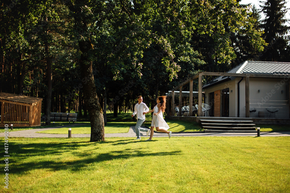 Fototapeta premium loving young couple having fun outdoors in summer sunny day. Man and woman are running near cafe in park. valentines day