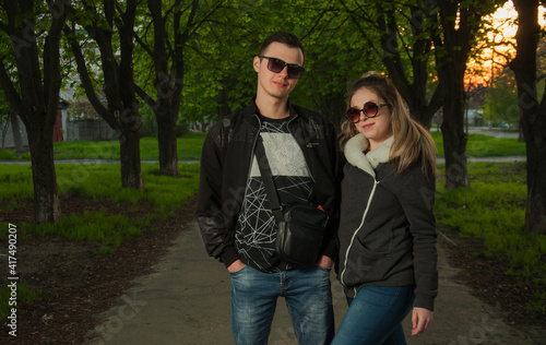 A couple in love, a girl and a guy together on the street in the spring against a background of greenery and flowers in jackets and jeans and in sunglasses