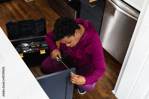 Black woman does DIY home repair on kitchen cabinet