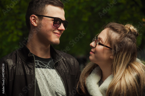 A couple in love, a girl and a guy together on the street in the spring against a background of greenery and flowers in jackets and jeans and in sunglasses