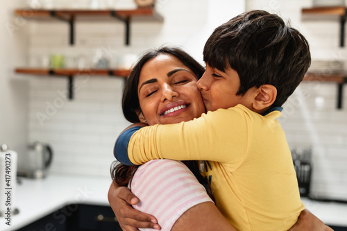 Smiling Indian mom embracing son at home in kitchen