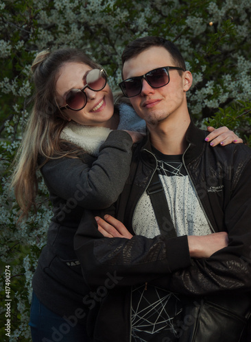 A couple in love, a girl and a guy together on the street in the spring against a background of greenery and flowers in jackets and jeans and in sunglasses