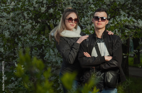 A couple in love, a girl and a guy together on the street in the spring against a background of greenery and flowers in jackets and jeans and in sunglasses