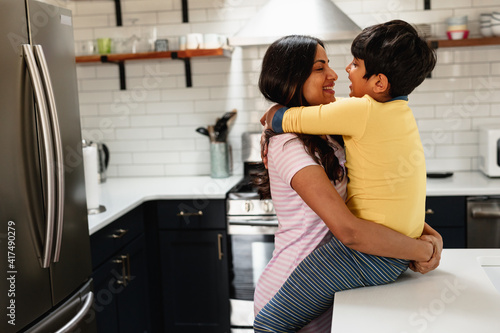 Smiling Indian mom embracing son at home in kitchen