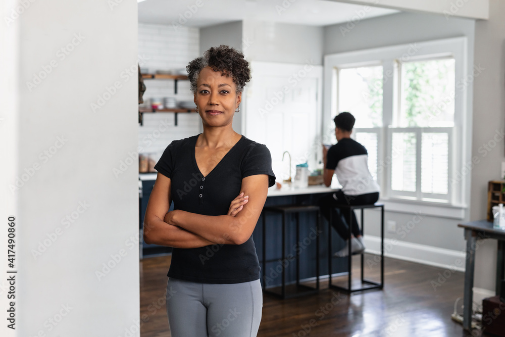 Portrait of Black mother with son in the background in kitchen on the phone Portrait of Black mother with son in the background in kitchen on the phone