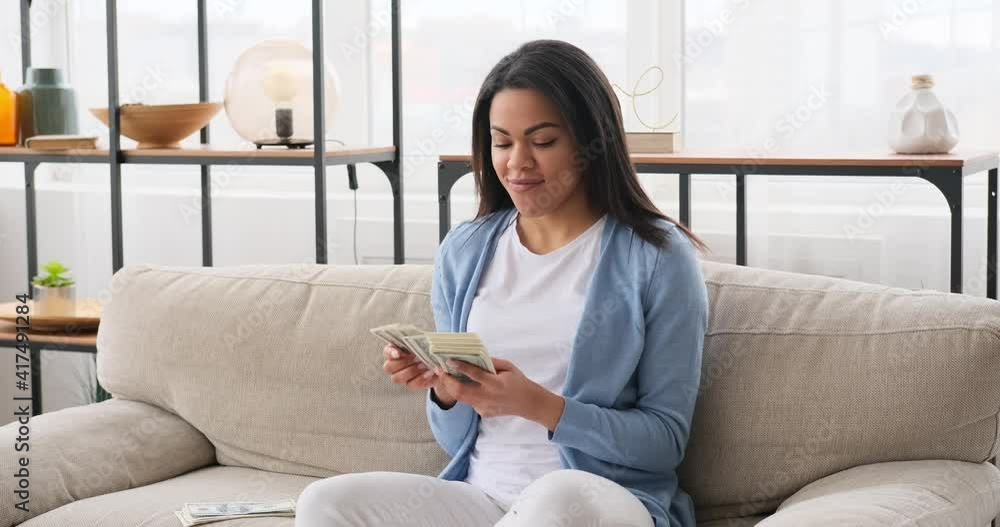 Thoughtful woman counting money sitting on sofa at home Thoughtful woman counting money sitting on sofa at home