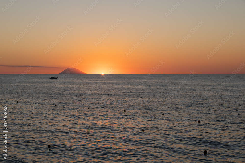 Amazing view of the Stromboli Volcano at sunset, wit the sun going down and amazing sea and sky colors. View form the coast of Calabria, Italy, in the touristic destination of Tropea.