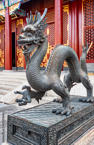 Beijing, China - April 29, 2010: Summer Palace. Closeup of gray metal dragon statue in front of Red and golden Hall of Remembrance and Longevity.