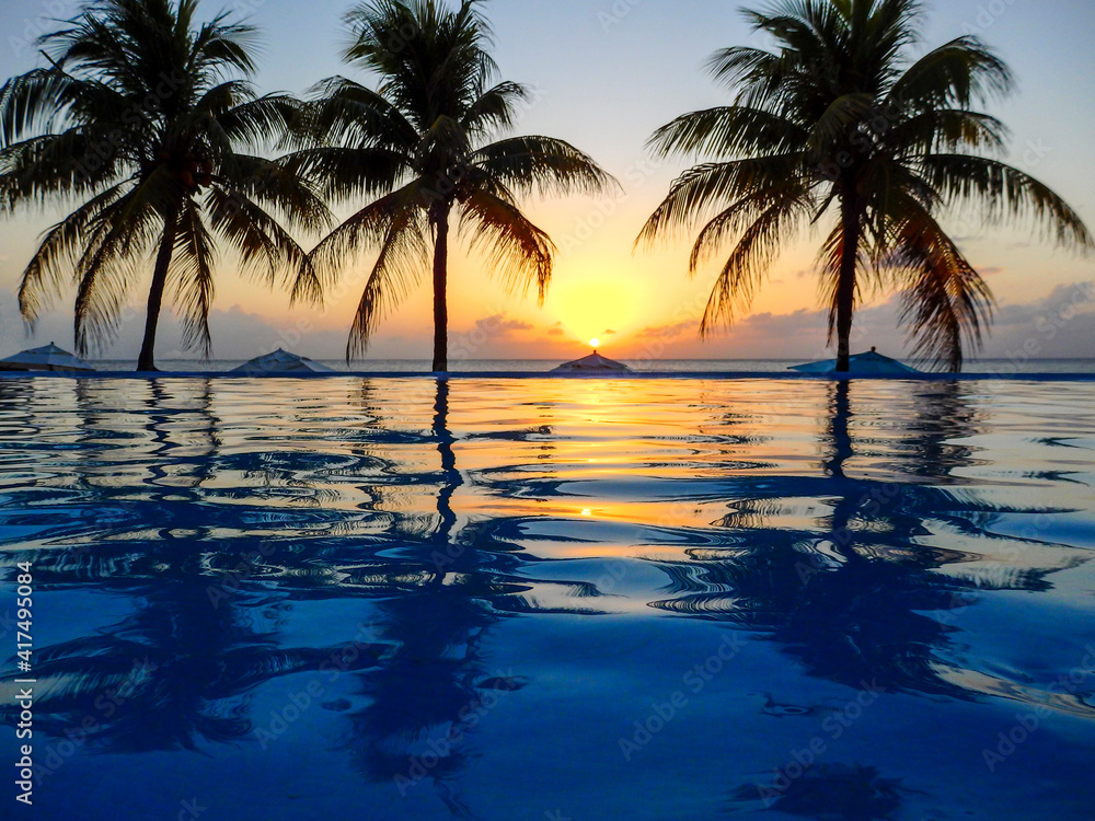 Caribbean, Honduras, Roatan. Infinity pool surrounded by palm trees at sunset.