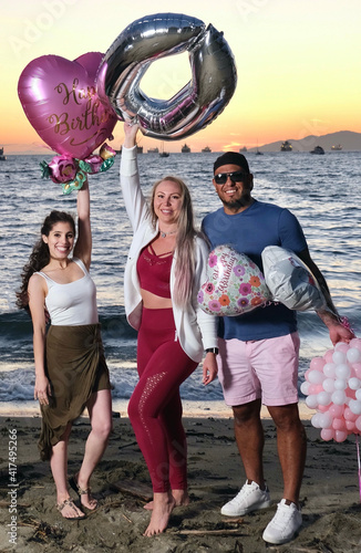 Group of young people celebration birthday with air balloons in hands. Second beach at sunset. Downtown Vancouver. British Columbia. Canada photo