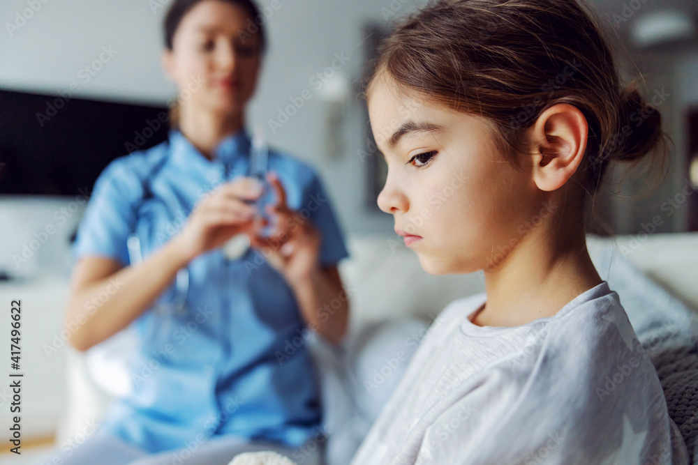 Nurse holding syringe with cure and preparing to give a shot to ill girl. Selective focus on girl who doesn't want to take injection. Nurse holding syringe with cure and preparing to give a shot to ill girl. Selective focus on girl who doesn't want to take injection.
