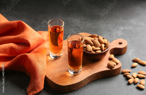 Board with glasses of almond liquor and nuts on dark background