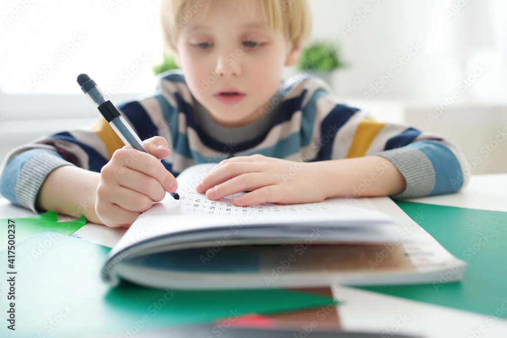 Elementary student boy doing homework at home. Child learning to count, solves arithmetic examples, doing exercises in workbook. Math tutorial. Preparing preschooler baby for school. Education Elementary student boy doing homework at home. Child learning to count, solves arithmetic examples, doing exercises in workbook. Math tutorial. Preparing preschooler baby for school. Education