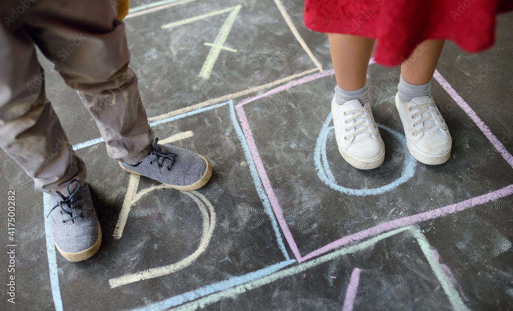 Closeup of little boy and girl legs and hop scotch drawn on asphalt. Child playing hopscotch game on playground outdoors on a sunny day. Kids having fun. Best friends