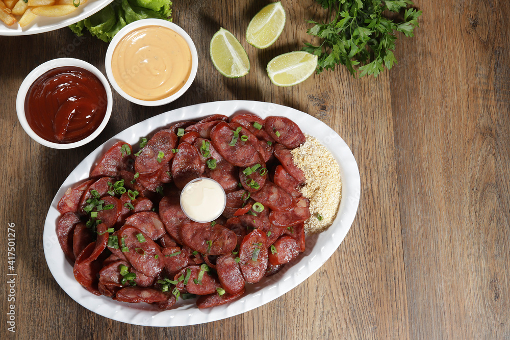 Portion of pepperoni sausage with lemon. Lettuce, green onion, ketchup and mayonnaise