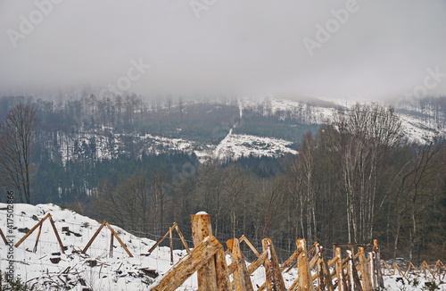 Foggy winter landscape - snowy glade with wood fence and foggy forest landscape in the background