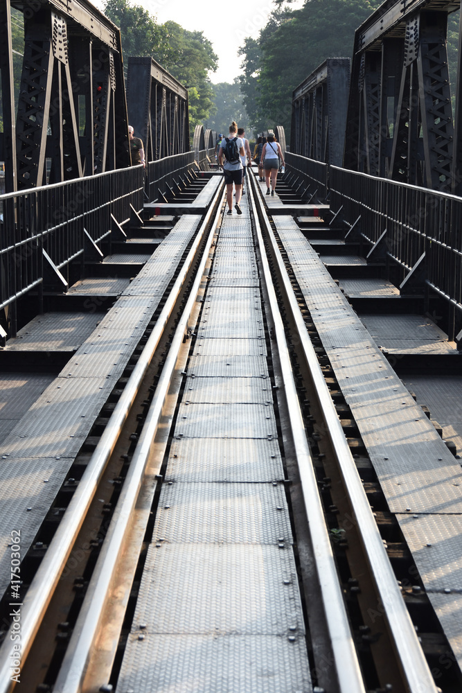 Tourists walking on the historic railroad tracks on the bridge of River Kwai in Kanchanaburi, Thailand Tourists walking on the historic railroad tracks on the bridge of River Kwai in Kanchanaburi, Thailand