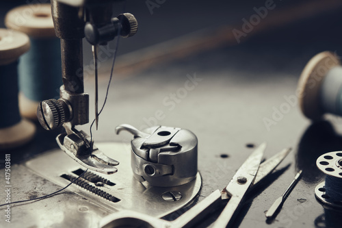 Close up on metal shuttle, foot of vintage sewing machine, scissors, spool of thread, sewing needles. Sewing items on working part of antique sewing machine.
