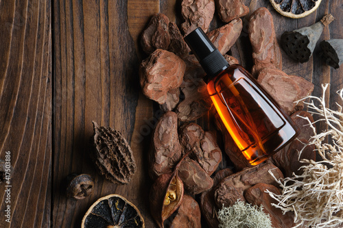 Bootle of oil, moisturizing lotion or other cosmetic product on wooden background with pine bark, moss, citrus, roots.  Mock up bottle of organic body treatment. Top view.