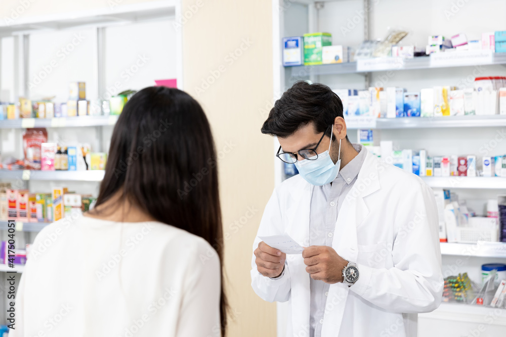 Middle eastern male pharmacist wearing protective hygienic mask to prevent infection selling medications to woman patient to prescription and making drug recommendations in modern pharmacy