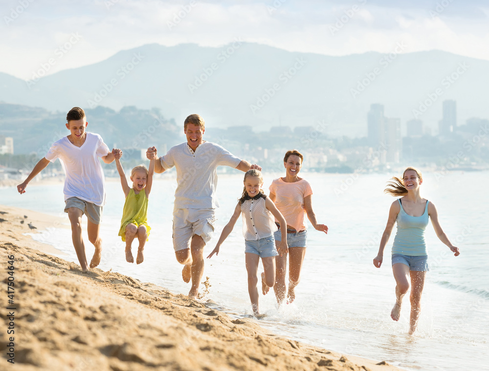 Large active family of six people happily running together on beach on summer day