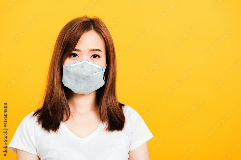 Asian happy portrait beautiful cute young woman standing wear t-shirt making mask protection from virus epidemic or air pollution looking camera isolated, studio shot yellow background with copy space Asian happy portrait beautiful cute young woman standing wear t-shirt making mask protection from virus epidemic or air pollution looking camera isolated, studio shot yellow background with copy space