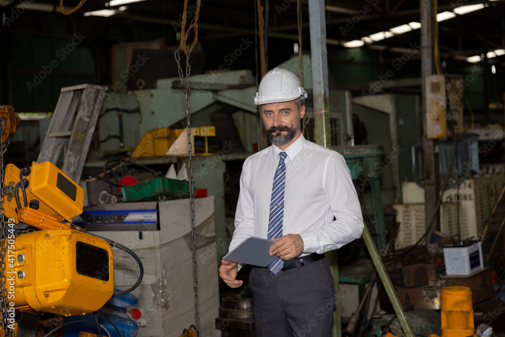 Male mechanical engineer or manager with hardhat uses a tablet to check the operation system in a factory Male mechanical engineer or manager with hardhat uses a tablet to check the operation system in a factory