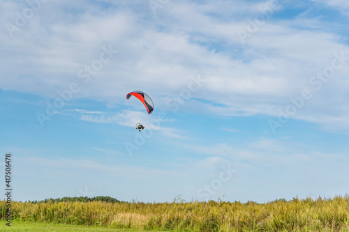Moto-paraglider on green grass with blue sky.