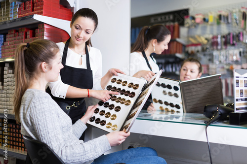 Young woman hairdresser edvise woman client about samples of hair dye in beauty showroom