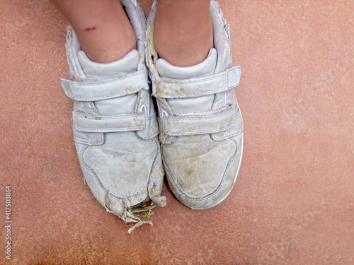 Foot in a damaged sport shoes of a poor child
