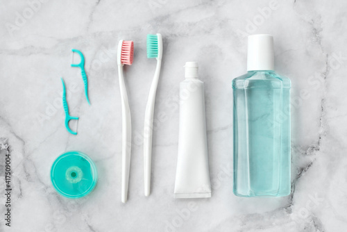 Set of pink and turquoise blue toothbrushes, toothpaste and other tools on marble background. Dental and health care concept. Top view, flat lay.
