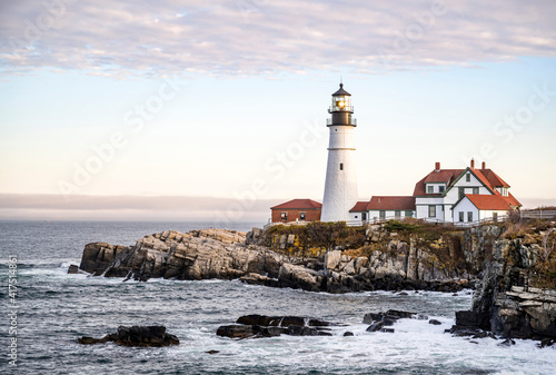 An operating lighthouse on a rocky promontory against the backdrop of a cloudy sky on the Atlantic coast in Portland Maine in New England