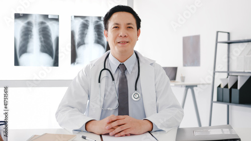 Confident young Asia male doctor in white medical uniform with stethoscope looking at camera and smiling while video conference call with patient in health hospital. Consulting and therapy concept.