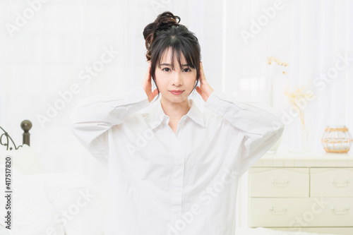 部屋で耳を塞ぐジェスチャーをする白いシャツを着た若い女性