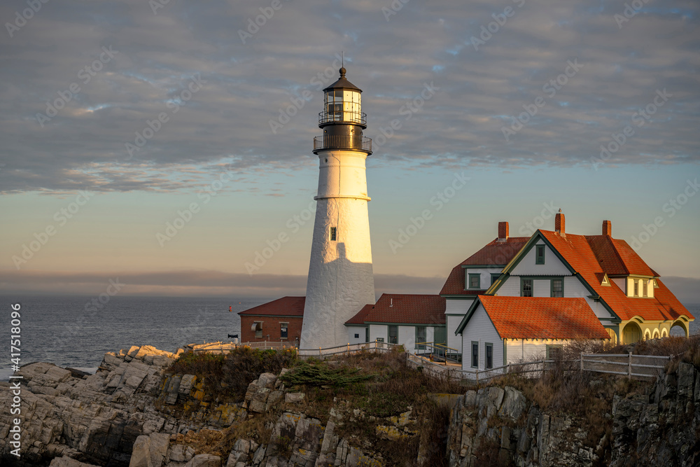 Operating Lighthouse Illuminated by the setting sun on a rocky promontory against a cloudy sky on the Atlantic coast in Portland Maine in New England