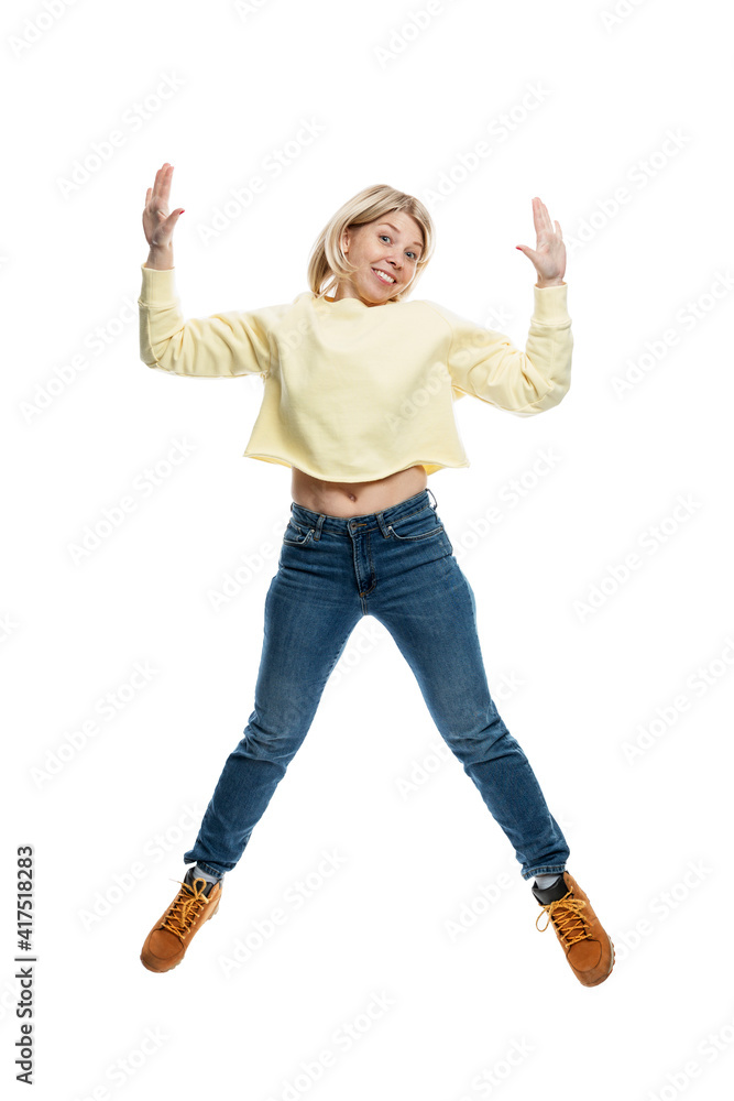 Young woman jumping. Smiling blonde in a yellow sweater and jeans. Movement and energy. Isolated on white background. Vertical. Young woman jumping. Smiling blonde in a yellow sweater and jeans. Movement and energy. Isolated on white background. Vertical.
