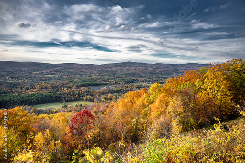 Scenic Autumn Maple Grove and Valley City in Sunlight and Thunderstorm Skies in the rolling hills of Vermont
