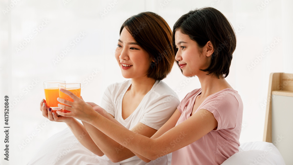 Couple adults lesbians asian women very pretty with short hair hold orange juice in cup glass smile and feeling happy but hasn't look at camera sitting on bed and in room on morning Couple adults lesbians asian women very pretty with short hair hold orange juice in cup glass smile and feeling happy but hasn't look at camera sitting on bed and in room on morning
