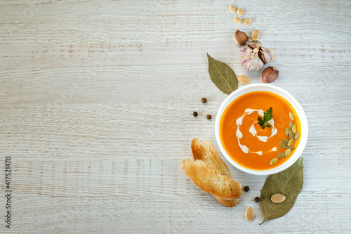 Vegetarian pumpkin cream soup in a white bowl decorated with seeds and herbs on a light background