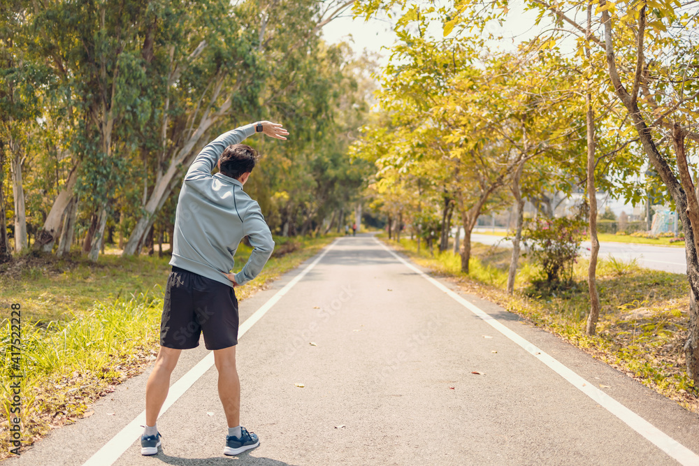 young man stretching in the park before running. Young man workout before fitness training at the park. Healthy and exercise young man warming up on the road beside the forest. young man stretching in the park before running. Young man workout before fitness training at the park. Healthy and exercise young man warming up on the road beside the forest.