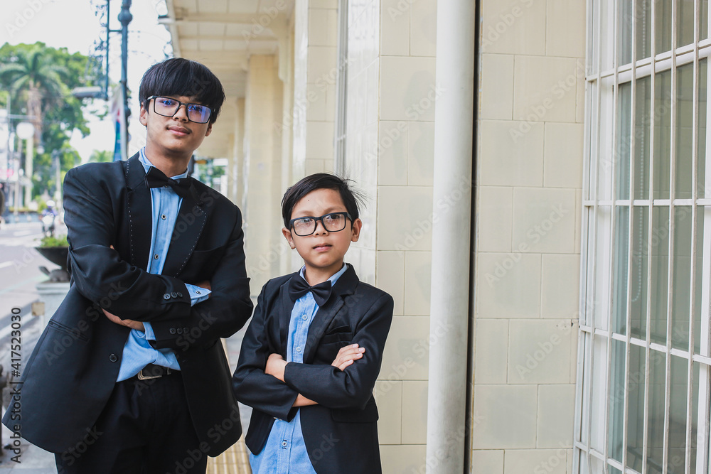 Fototapeta premium Two brothers with vintage office look, wearing glasses, black ribbon and black suit posing in front of the camera while crossed arm