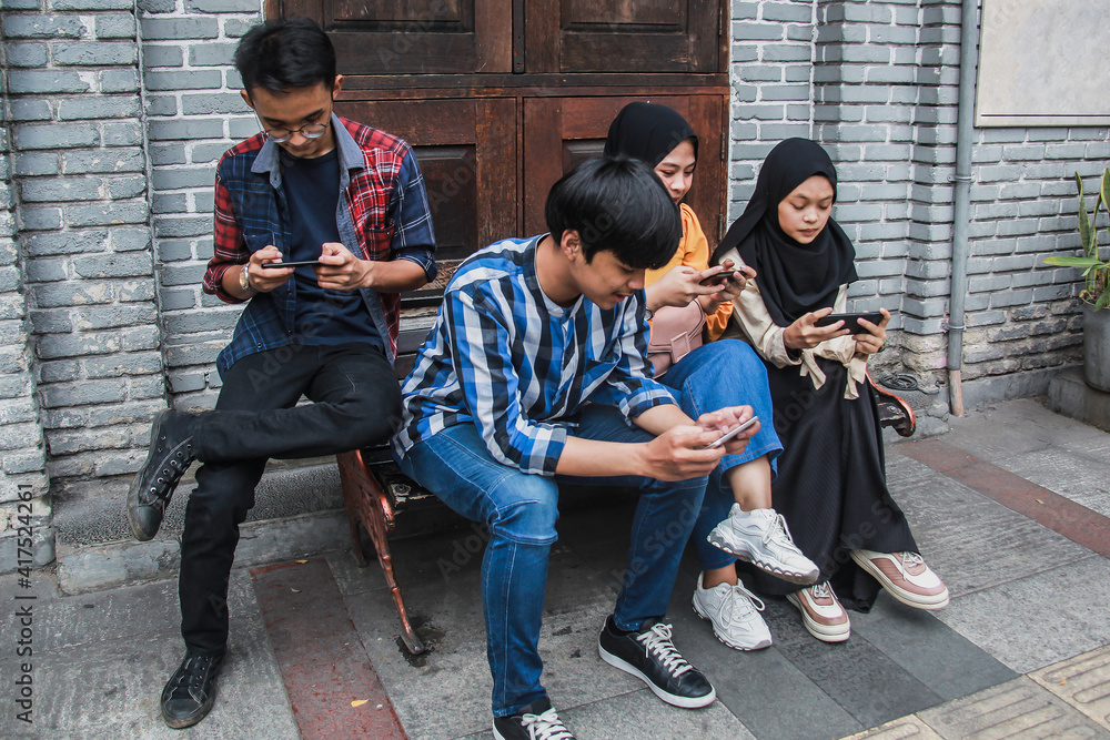 Fototapeta premium Youth addicted for the smartphone and social media networks. Young people sitting in a bench holding and watching their own smartphones