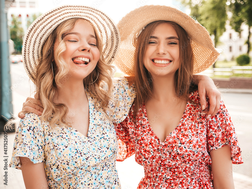 Two young beautiful smiling hipster female in trendy summer sundress.Sexy carefree women posing on the street background in hats. Positive models having fun and hugging
